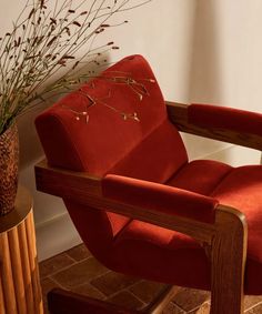 a red chair sitting next to a plant in a vase on top of a wooden table