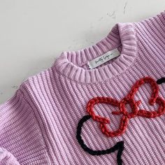 a pink sweater with black and red braids on the front, sitting on a white surface