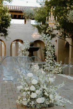 an outdoor ceremony with clear chairs and white flowers