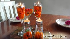 three wine glasses filled with orange flowers on a wooden table next to two white plates