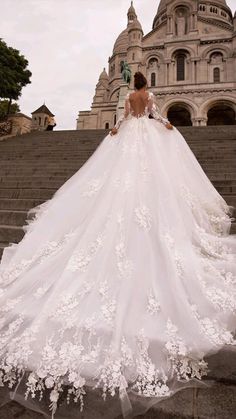 a woman in a white wedding dress standing on some steps with her back to the camera