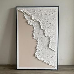 a white and black framed art piece on a wooden floor with a wall in the background