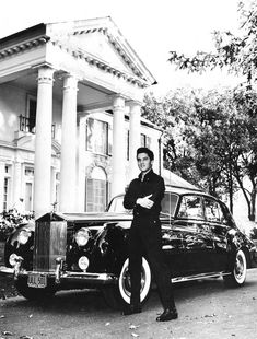 a black and white photo of a man standing next to a car in front of a house