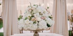 a vase filled with white and pink flowers sitting on top of a table next to drapes