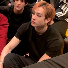 three young men sitting next to each other in front of a group of people wearing black shirts