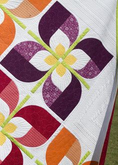 a woman holding up a colorful quilt on the grass