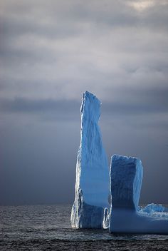 an iceberg floating in the ocean on a cloudy day