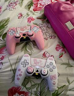 two video game controllers sitting on top of a bed next to a pink bag and purse