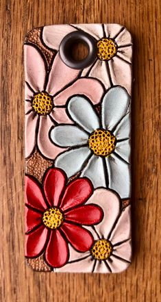 a phone case with flowers painted on it sitting on top of a wooden table next to a bottle opener