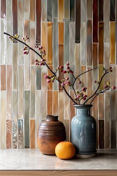 two vases with flowers in them sitting on a counter top next to an orange