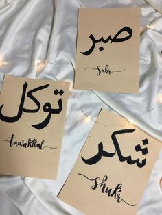 three arabic calligraphys are displayed on a sheet of paper with lights in the background