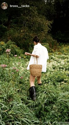 a woman walking through tall grass carrying a basket