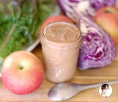 an apple and some vegetables on a cutting board next to a jar of peanut butter