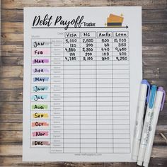 a printable debt planner with two pens and some other items next to it on a wooden table