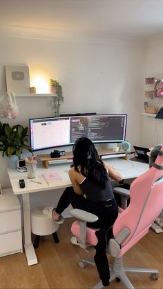 a woman sitting at a desk with two computer monitors and a pink chair in front of her