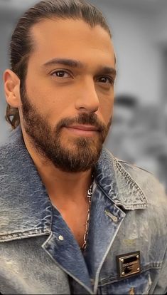 a man with long hair and a beard wearing a denim jacket is looking at the camera