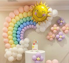 there is a cake and balloons on the table in front of this rainbow balloon wall