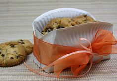 a cookie in a paper container with an orange ribbon around it and two cookies on the side