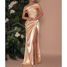 a woman standing in front of a plant wearing a gold dress with thigh high slit