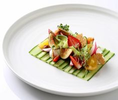 a white plate topped with cucumber, strawberries and radish slices