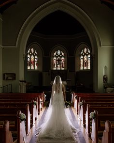 the bride is walking down the aisle in her wedding dress at the alter, looking towards the stained glass windows