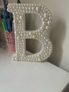 the letter b is made out of pearls and sits on a desk next to pens