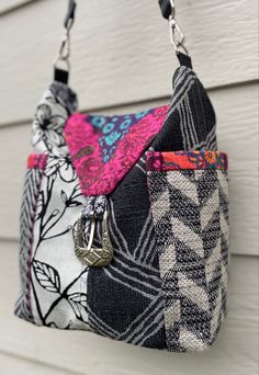 two purses hanging from the side of a house with white siding behind them and one has a pink flower on it