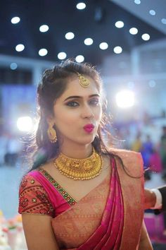 a woman in a pink sari with gold jewelry on her neck and chest, looking off to the side