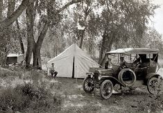 an old car parked next to a tent in the woods