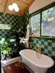 a bath tub sitting next to a window in a room with green tiles on the walls