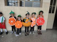 five children in costumes holding oranges and grapefruits standing next to a wall