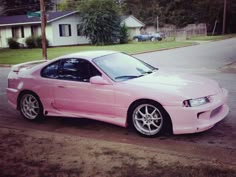 a pink sports car parked on the side of the road in front of a house