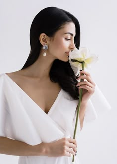 a woman in a white dress holding a flower and looking down at her left shoulder