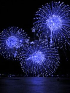 blue fireworks are lit up in the night sky over water and boats on the water