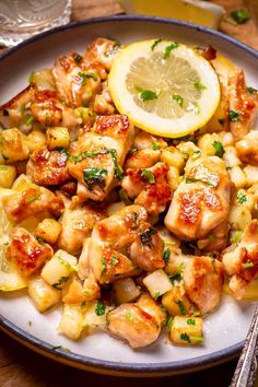 a white plate topped with chicken and pineapples next to a lemon wedge on top of a wooden table