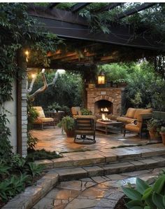 an outdoor fireplace and seating area with lights on the patio, surrounded by greenery