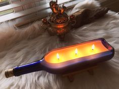 three lit candles in a blue glass container on a white fur covered floor next to a window