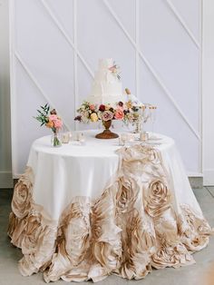 a table topped with a white cake covered in ruffles next to a vase filled with flowers