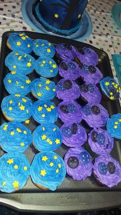 cupcakes with blue frosting and yellow stars are on a baking tray next to a cake