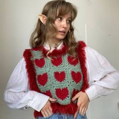 a woman wearing a red and green crocheted sweater with hearts on the chest