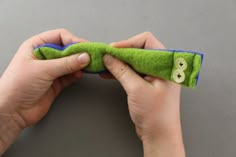 two hands are holding a green object with buttons on it and the other hand is sewing