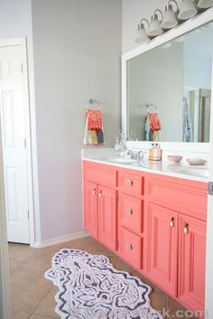 a bathroom with pink cabinets and white counter tops, rugs on the floor and a large mirror over the sink