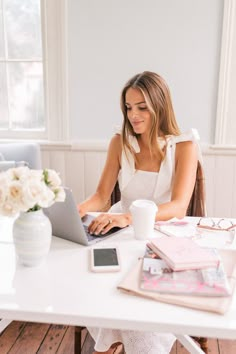 a woman sitting at a table with a laptop and coffee in front of her,