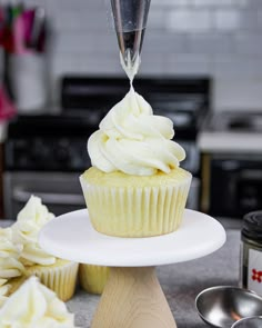 a cupcake with white frosting being poured into it on a cake stand next to other cupcakes