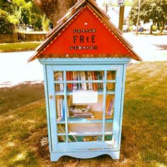 a blue book case with a red roof on the grass in front of a tree