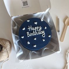 a blue birthday cake with white hearts on it in a box next to yarn and scissors