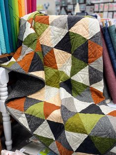 a quilted blanket sitting on top of a white chair next to colorful fabrics in the background