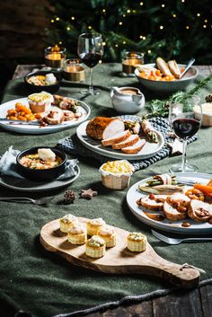 a table topped with plates of food next to a glass of wine and christmas tree