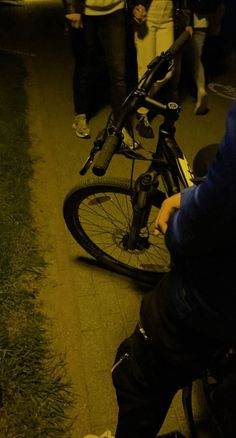 a man sitting on the ground next to a bike with people standing around it at night