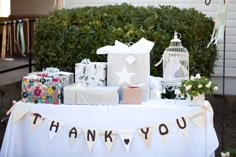 a white table topped with lots of gift bags and presents under a thank you sign